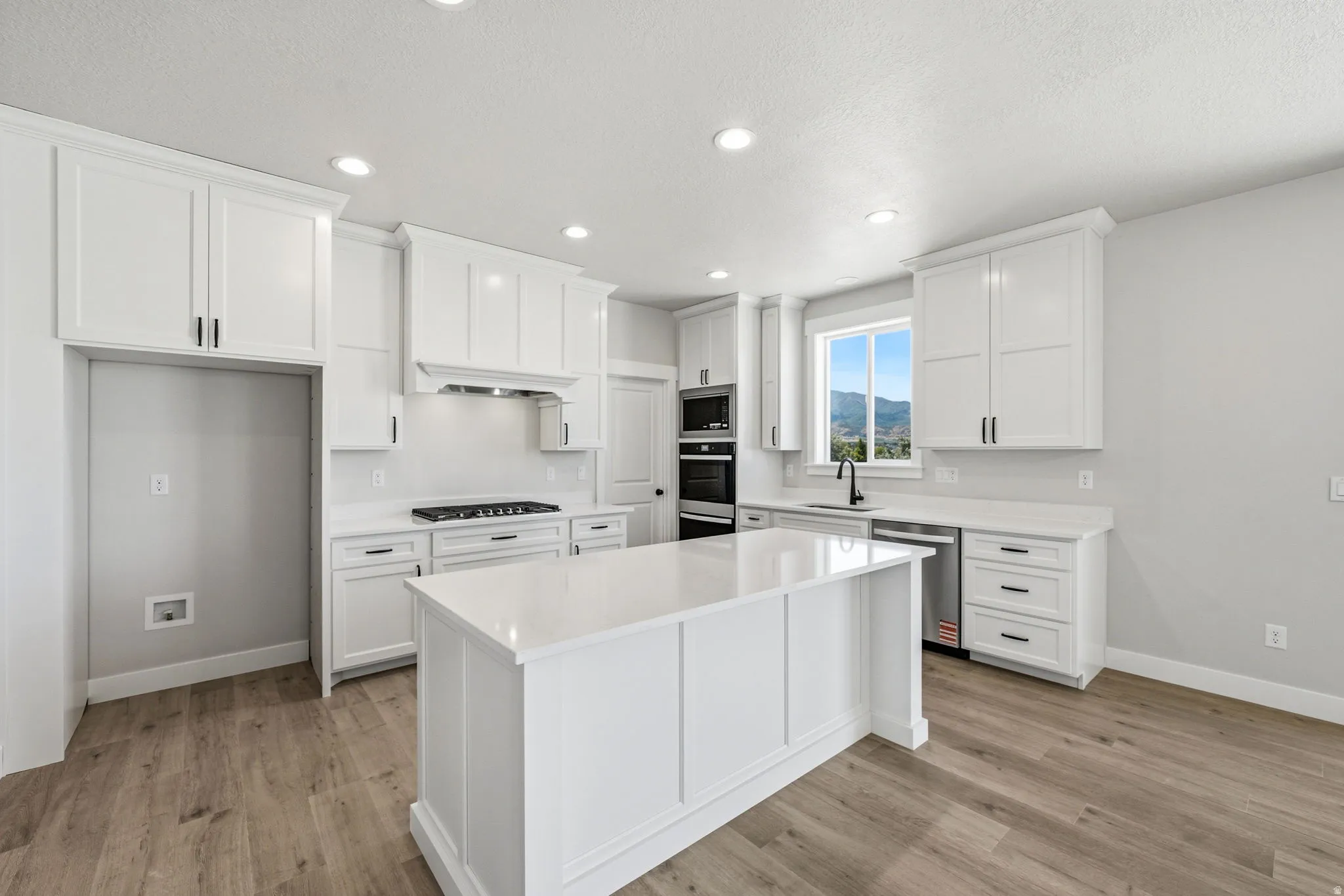 Modern kitchen featuring a central island with a solid surface countertop, white shaker cabinetry, recessed lighting, wood-finish flooring, and a built-in double oven