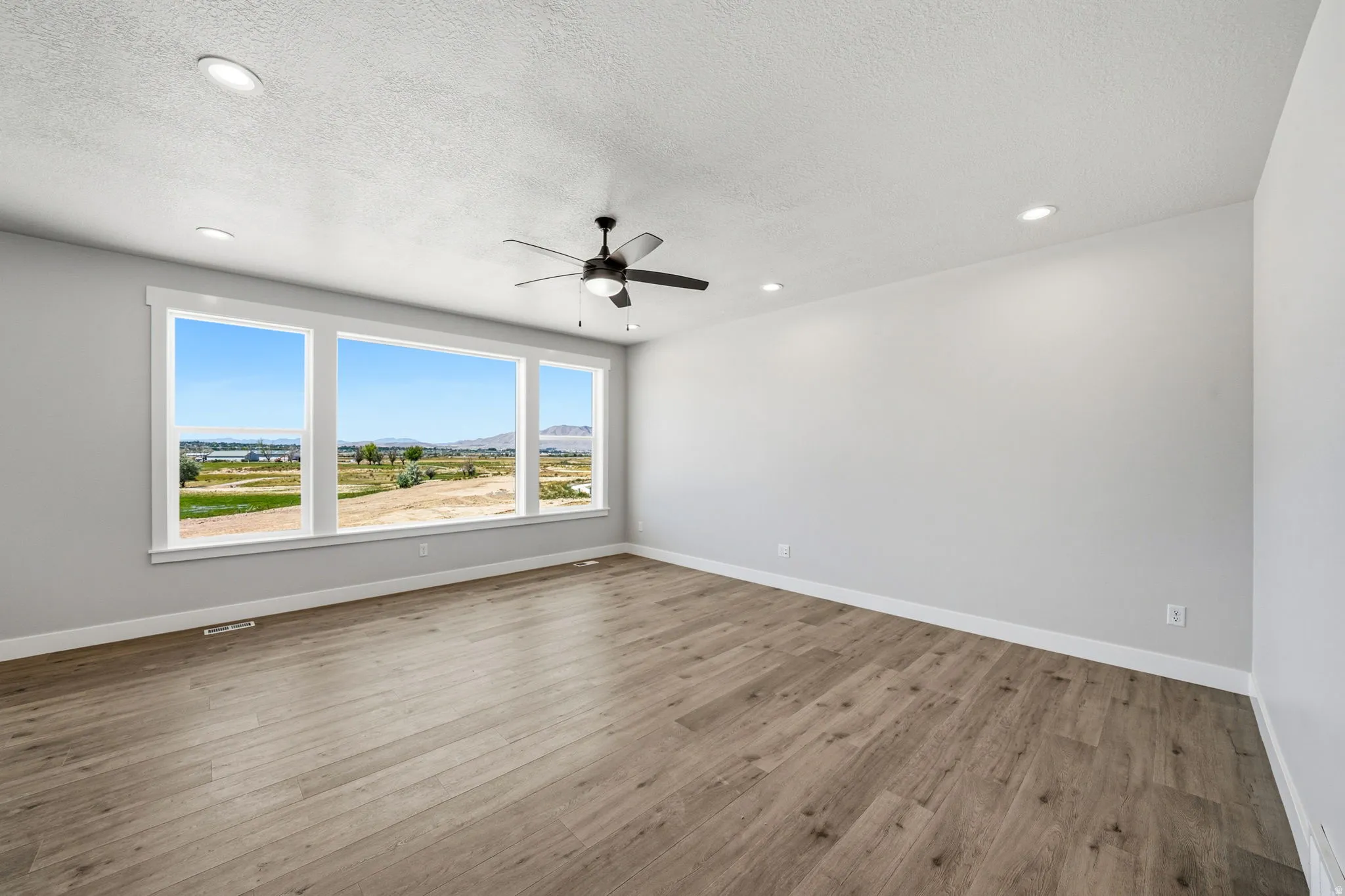 Expansive triple window offering extensive natural scenery, paired with recessed lighting, a ceiling fan, and wood-finish flooring