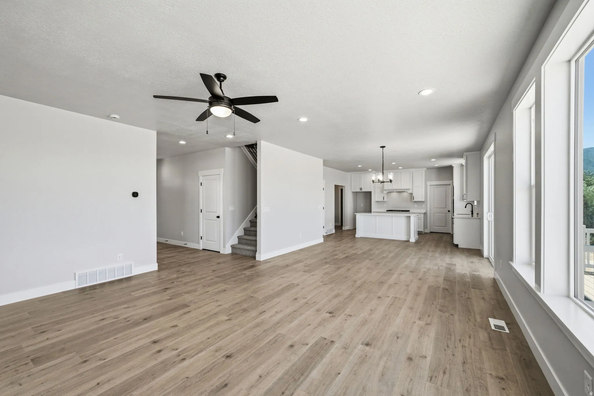 Open concept living space featuring wood-finish flooring throughout, a modern ceiling fan, recessed lighting, and large windows