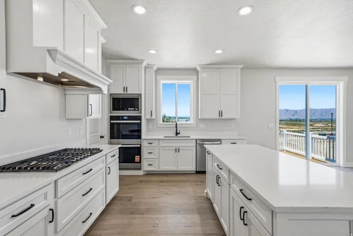 Contemporary kitchen featuring white cabinetry, a large center island with a stone countertop, stainless steel appliances including a wall oven and microwave, a gas range with an ornate range hood, and wood-finish flooring