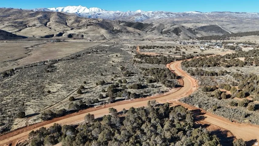 Expansive undeveloped land with a winding red dirt road, surrounded by natural vegetation and distant snow-capped mountains