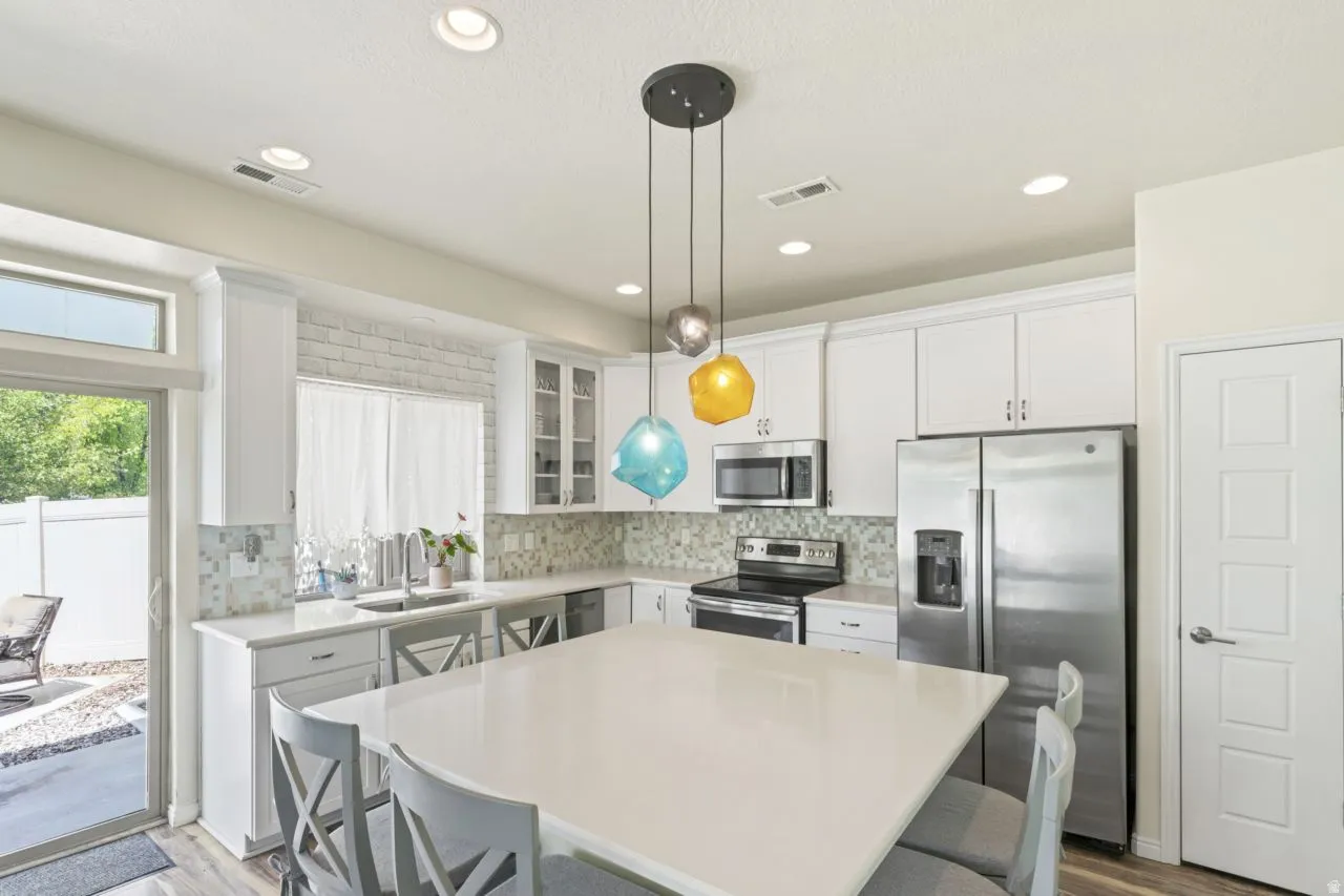 Kitchen featuring a kitchen breakfast bar, stainless steel appliances, white cabinets, light wood-style floors, and a kitchen island