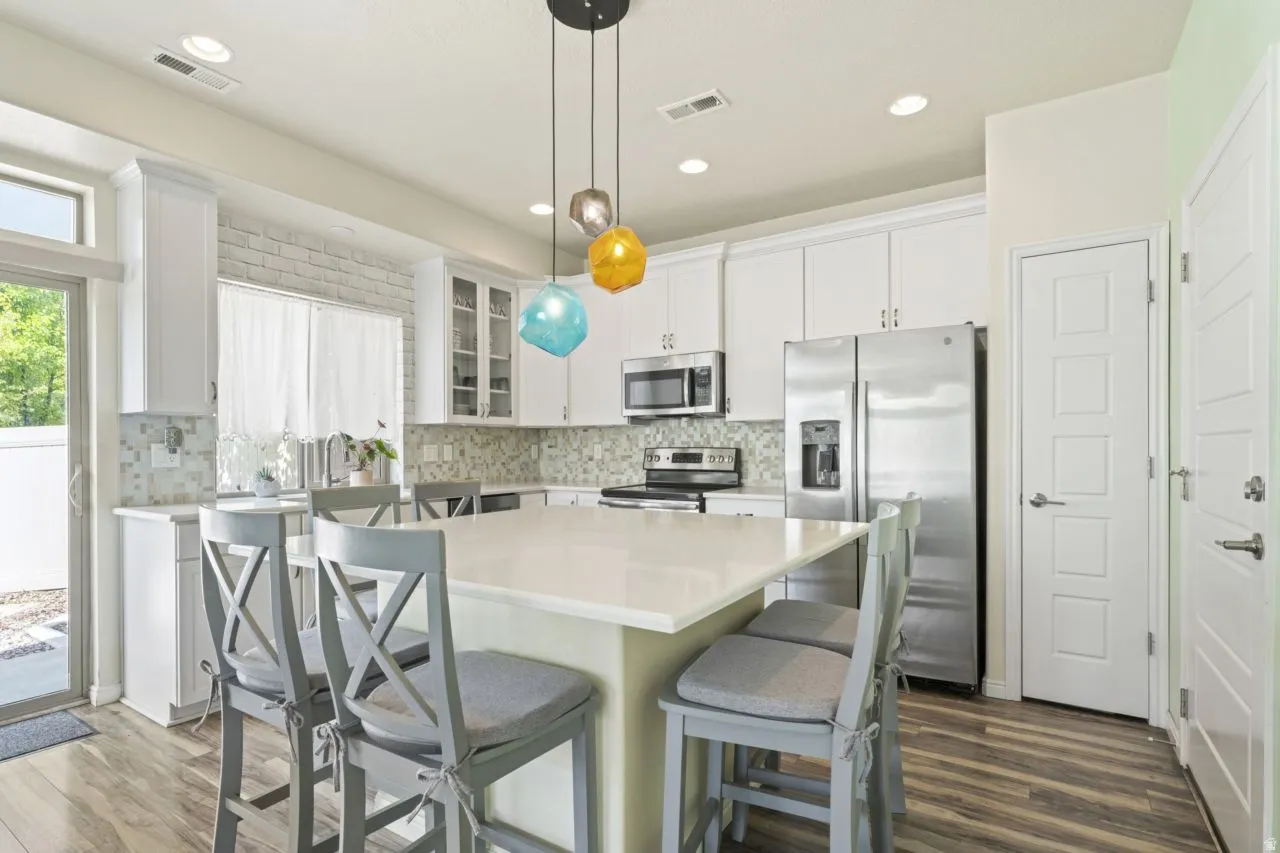 Kitchen featuring stainless steel appliances, white cabinetry, pendant lighting, a center island, and glass insert cabinets