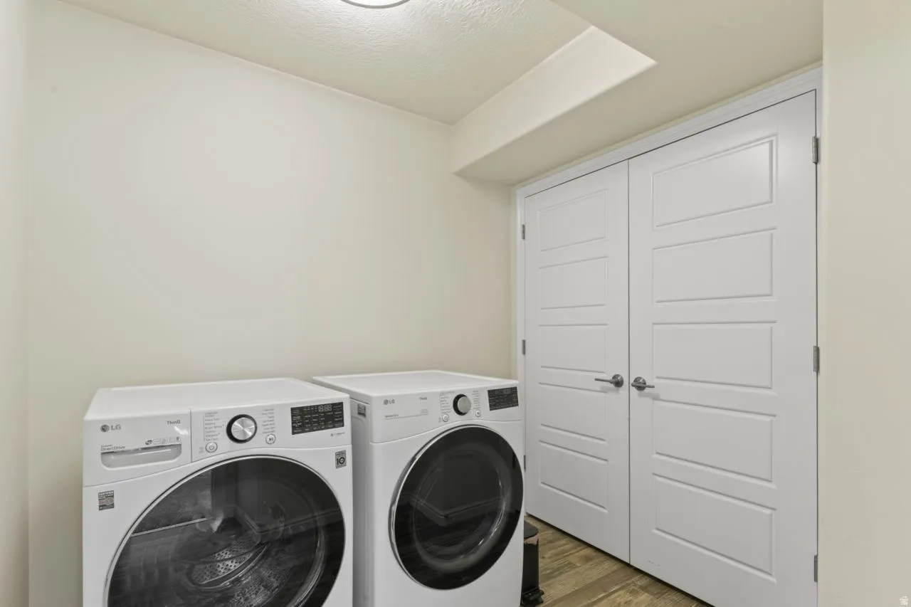 Laundry room with washing machine and dryer, a textured ceiling, and wood finished floors