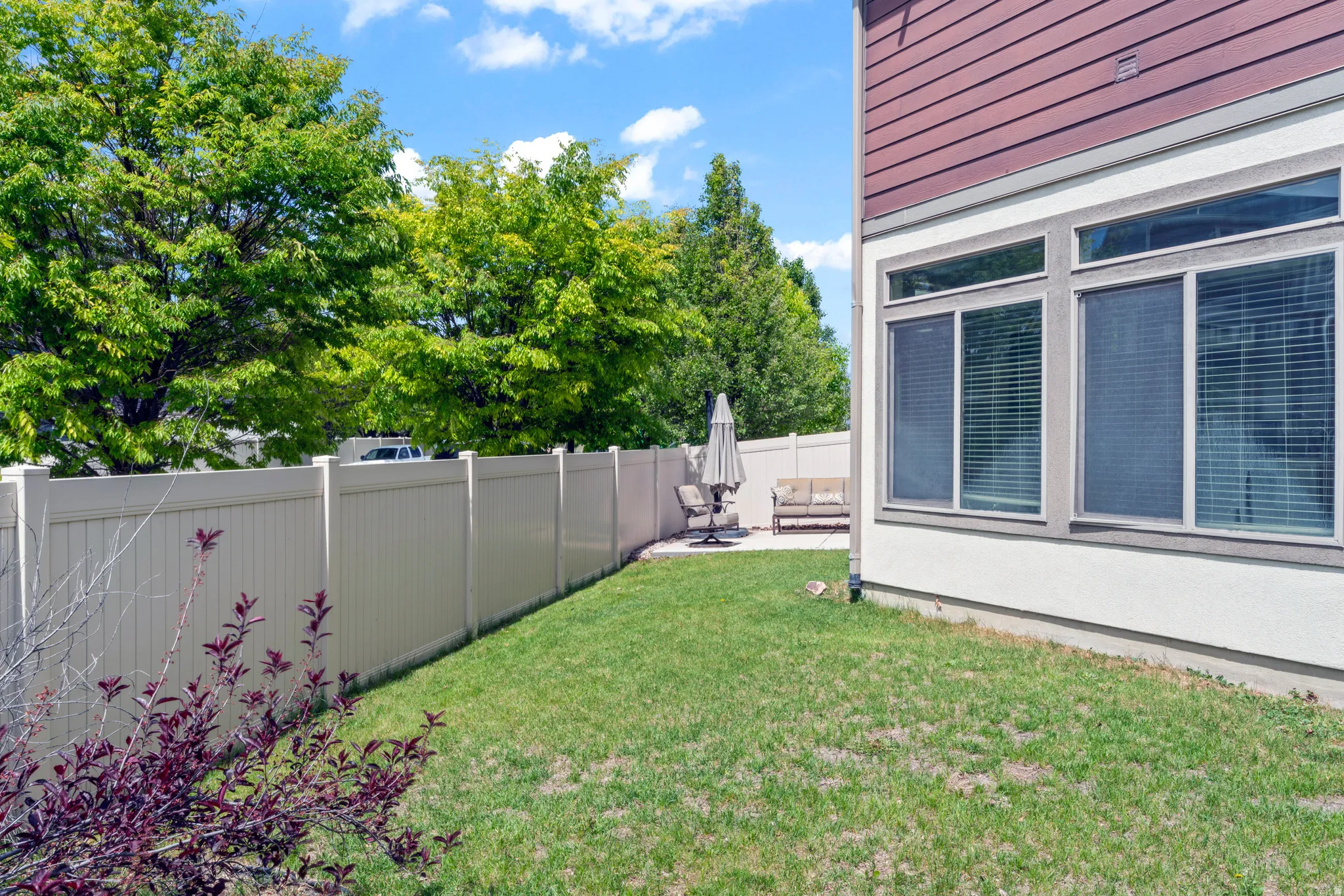 Manicured lawn area featuring a beige privacy fence and mature perimeter trees