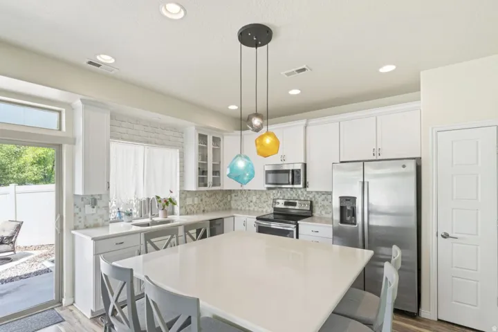 Kitchen featuring a kitchen breakfast bar, stainless steel appliances, white cabinets, light wood-style floors, and a kitchen island