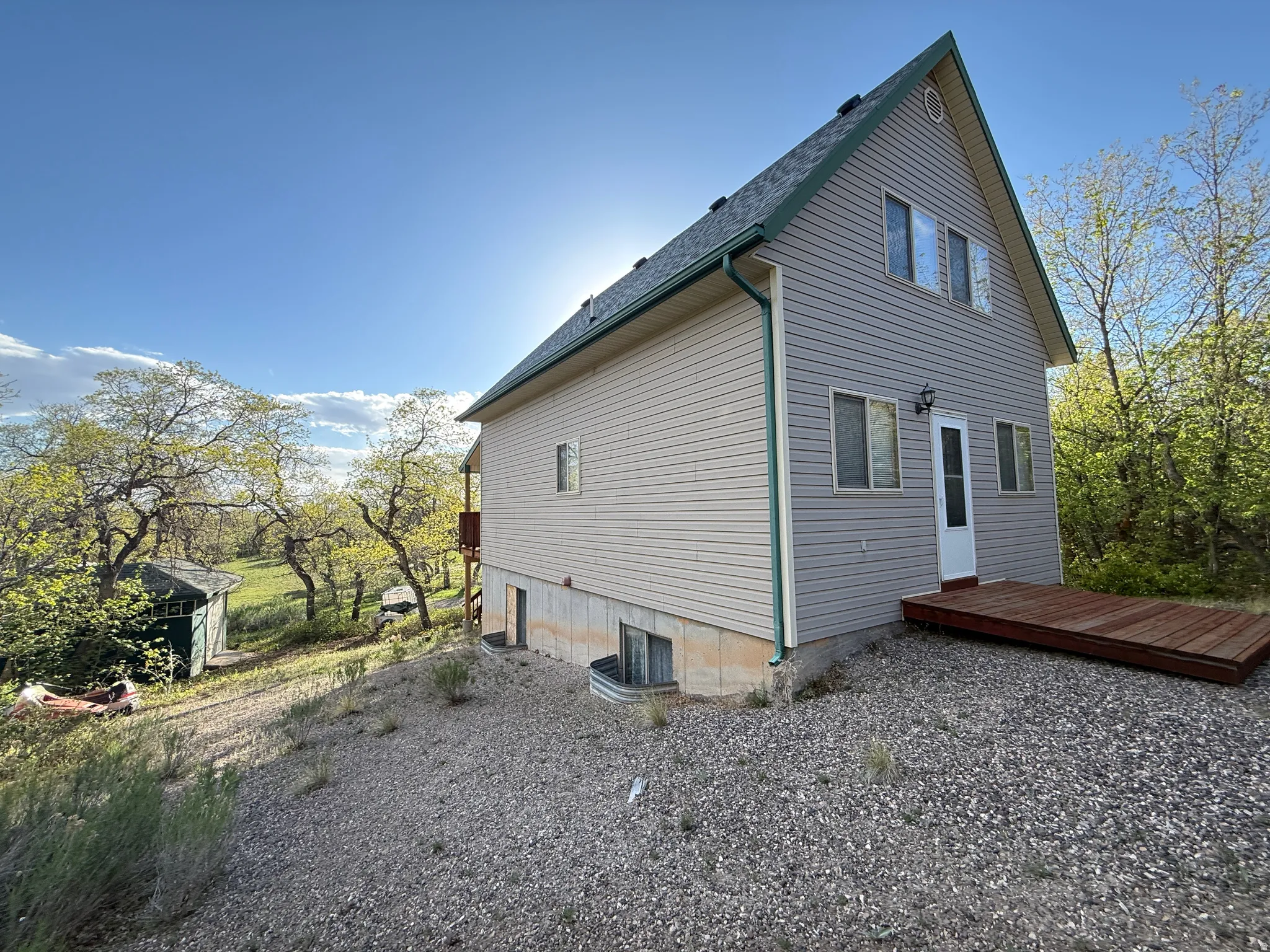 Two-story residence featuring light gray siding with green trim, a dark green shingle roof, and a gravel-covered yard