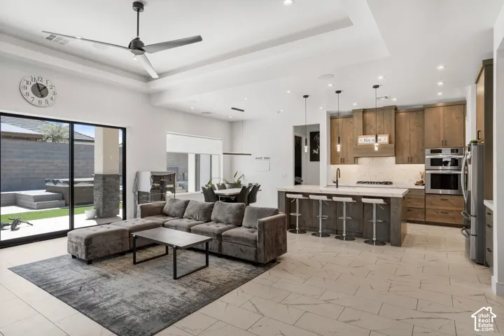 Living area with a tray ceiling, a ceiling fan, recessed lighting, and light marble finish flooring