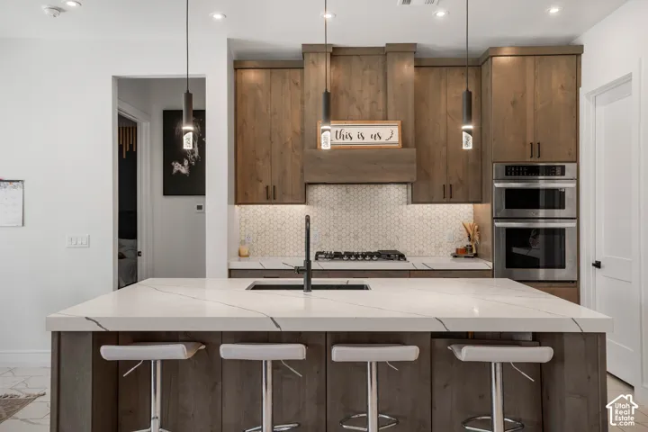 Kitchen featuring light stone countertops, a breakfast bar, a center island with sink, and decorative backsplash