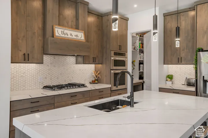 Kitchen with tasteful backsplash, a kitchen island with sink, stainless steel appliances, and light stone countertops