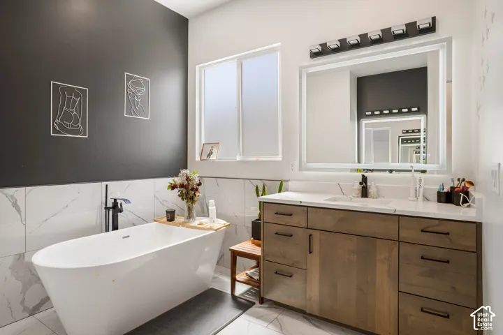 Full bathroom featuring vanity, a freestanding bath, tile walls, wainscoting, and light marble finish floors