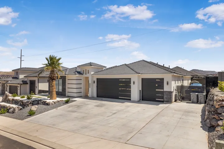 View of front of property featuring a garage, stone siding, concrete driveway, stucco siding, and a tiled roof