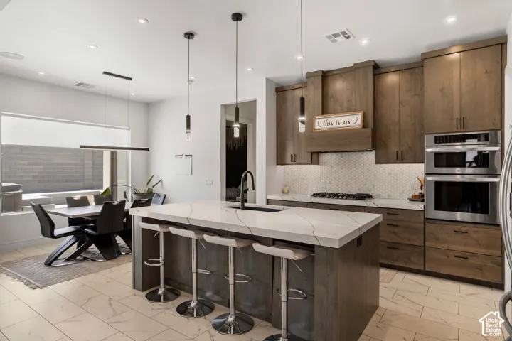 Kitchen featuring a kitchen bar, pendant lighting, a center island with sink, and modern cabinets