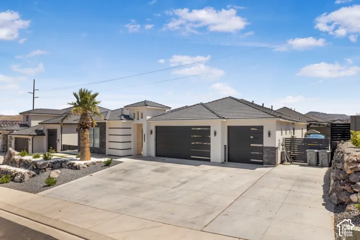 View of front of property featuring a garage, stone siding, concrete driveway, stucco siding, and a tiled roof