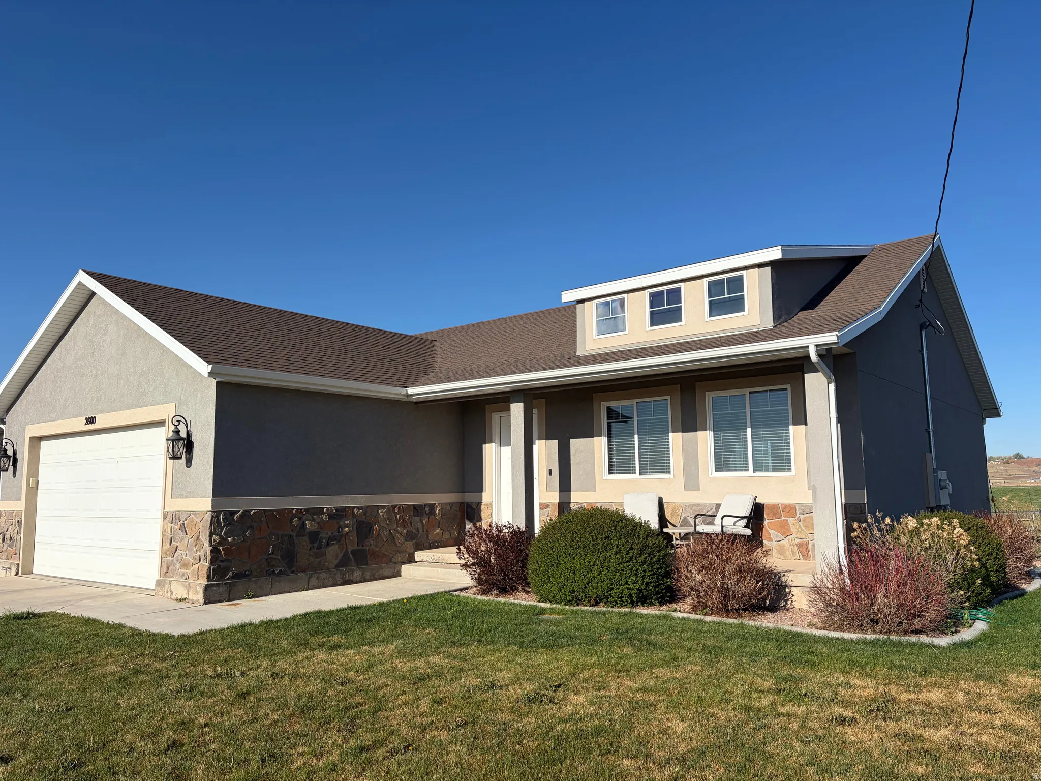 Single story home featuring stone siding, stucco siding, a front yard, a garage, and concrete driveway
