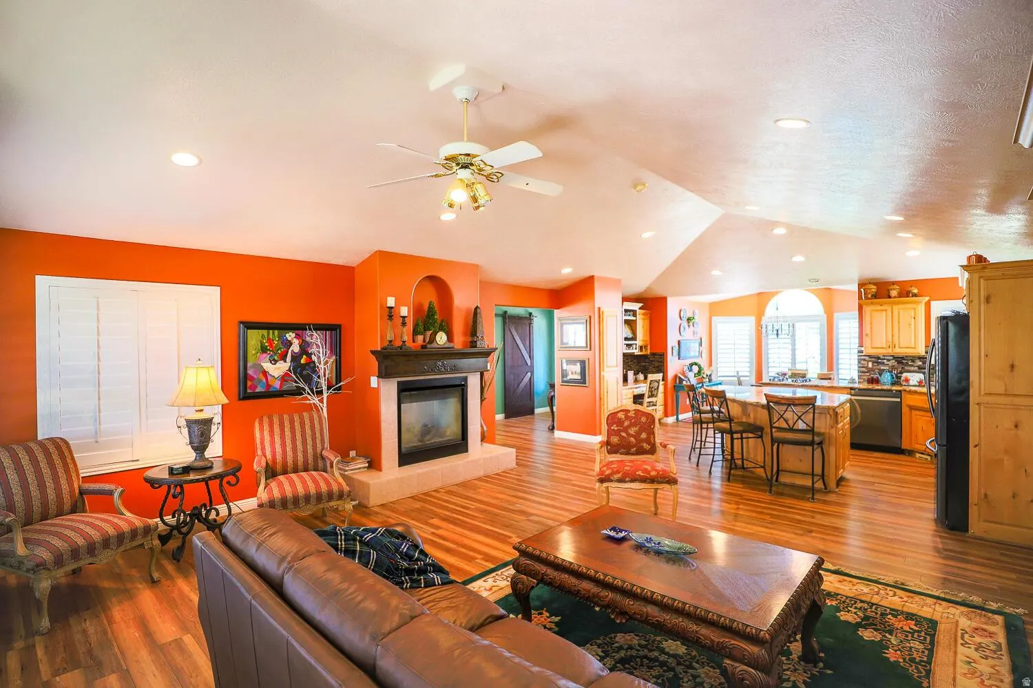 Living area featuring light wood-style flooring, ceiling fan, a glass covered fireplace, lofted ceiling, and recessed lighting