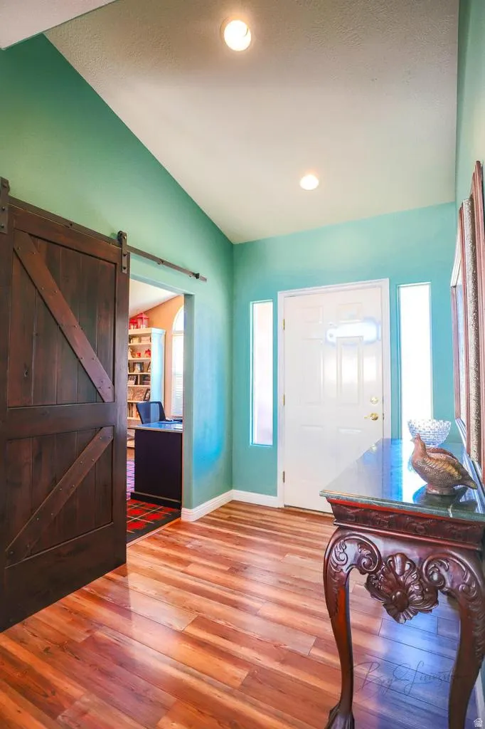 Entrance foyer with vaulted ceiling, wood finished floors, a barn door, and recessed lighting