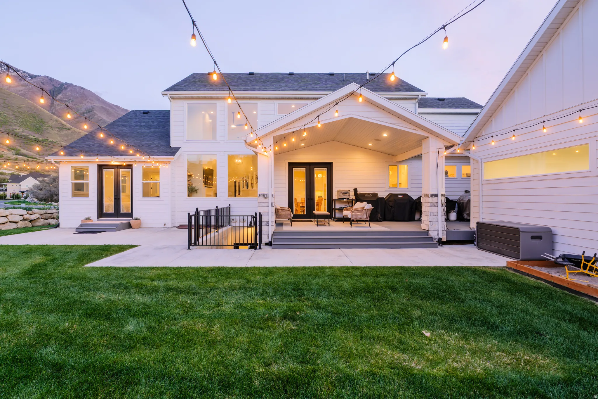Back of property at dusk featuring french doors, a yard, a patio, and roof with shingles
