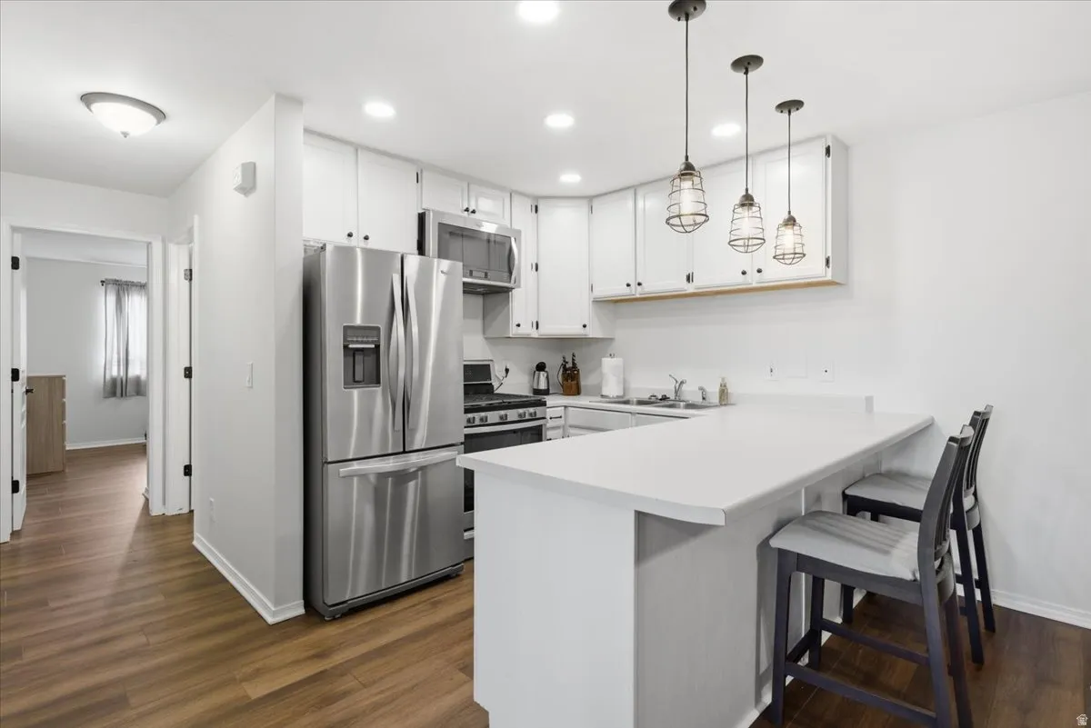 Kitchen featuring stainless steel appliances, light countertops, a kitchen bar, white cabinets, and a peninsula