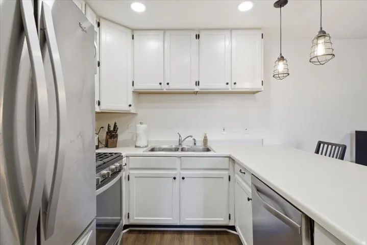 Kitchen featuring stainless steel appliances, white cabinets, light countertops, and pendant lighting