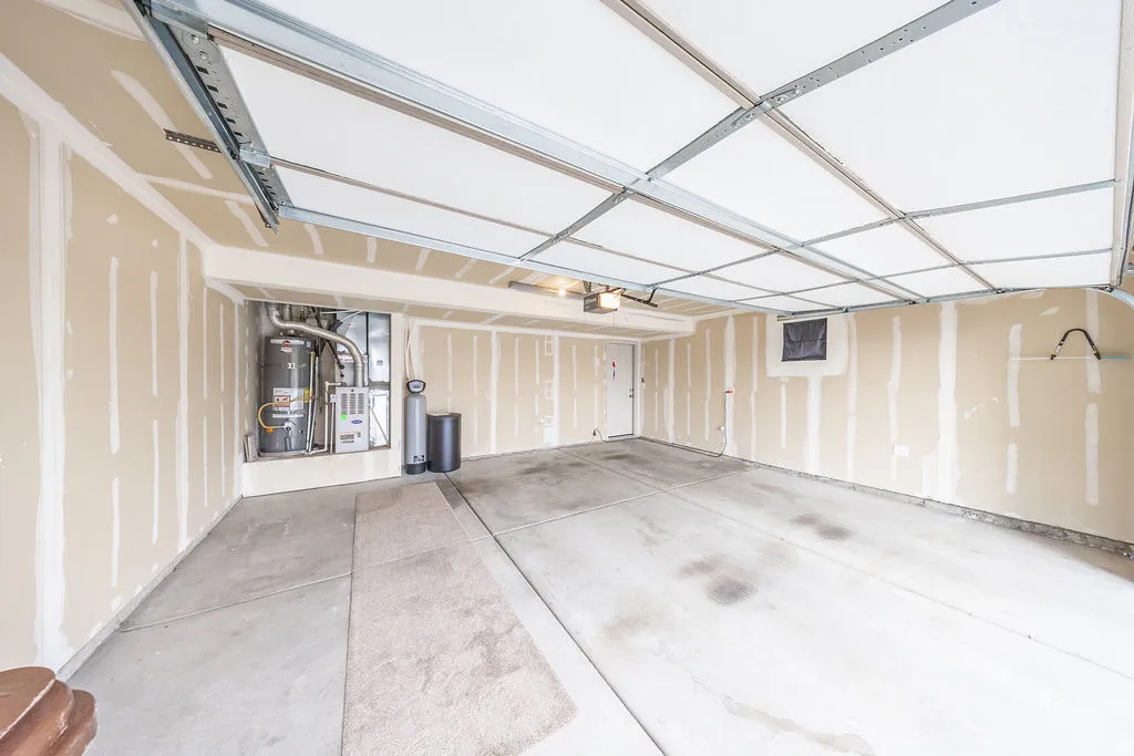Spacious garage featuring concrete flooring, unpainted drywall, exposed ceiling joists, and a water heater installation