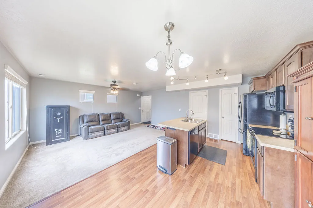 Open-concept living area featuring wood-finish flooring, a kitchen island with integrated sink, black appliances, and neutral-toned cabinetry
