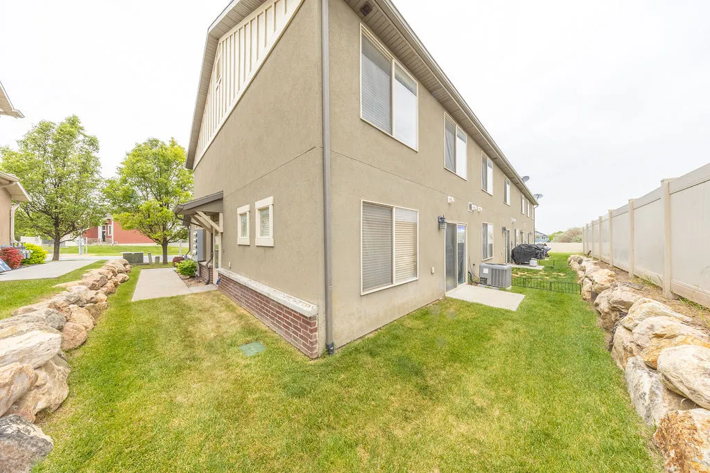 Rear exterior featuring stucco siding, brick detailing, a private patio, and a grass lawn bordered by rock landscaping