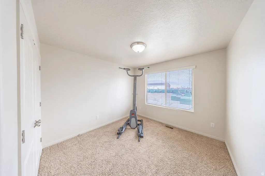 3rd bedroom featuring neutral carpeting, white painted walls, a window with horizontal blinds, a white door with silver-toned hardware, and a ceiling-mounted light fixture