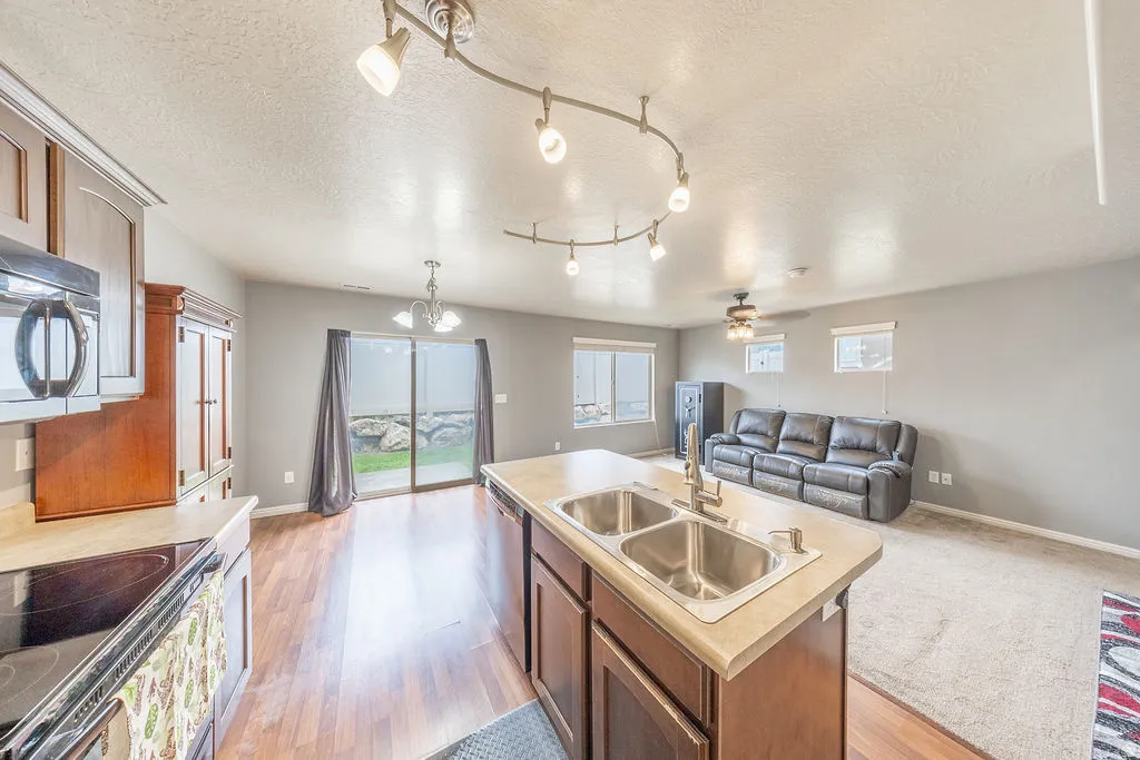 Open-concept living space featuring a kitchen island with a double basin sink, track lighting, wood-finish flooring, and a sliding glass door for outdoor access
