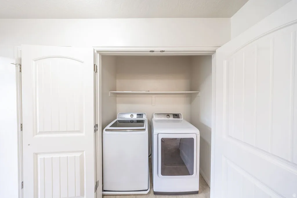 Laundry closet featuring a built-in shelf, white paneled bifold doors, and light-toned flooring