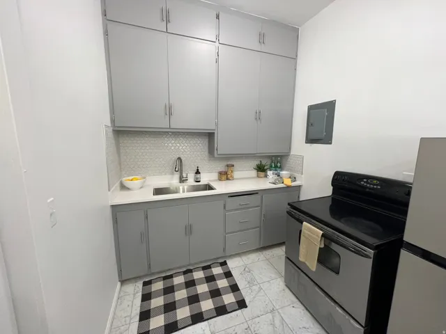 Kitchen featuring black range with electric stovetop, gray cabinetry, freestanding refrigerator, light countertops, and electric panel
