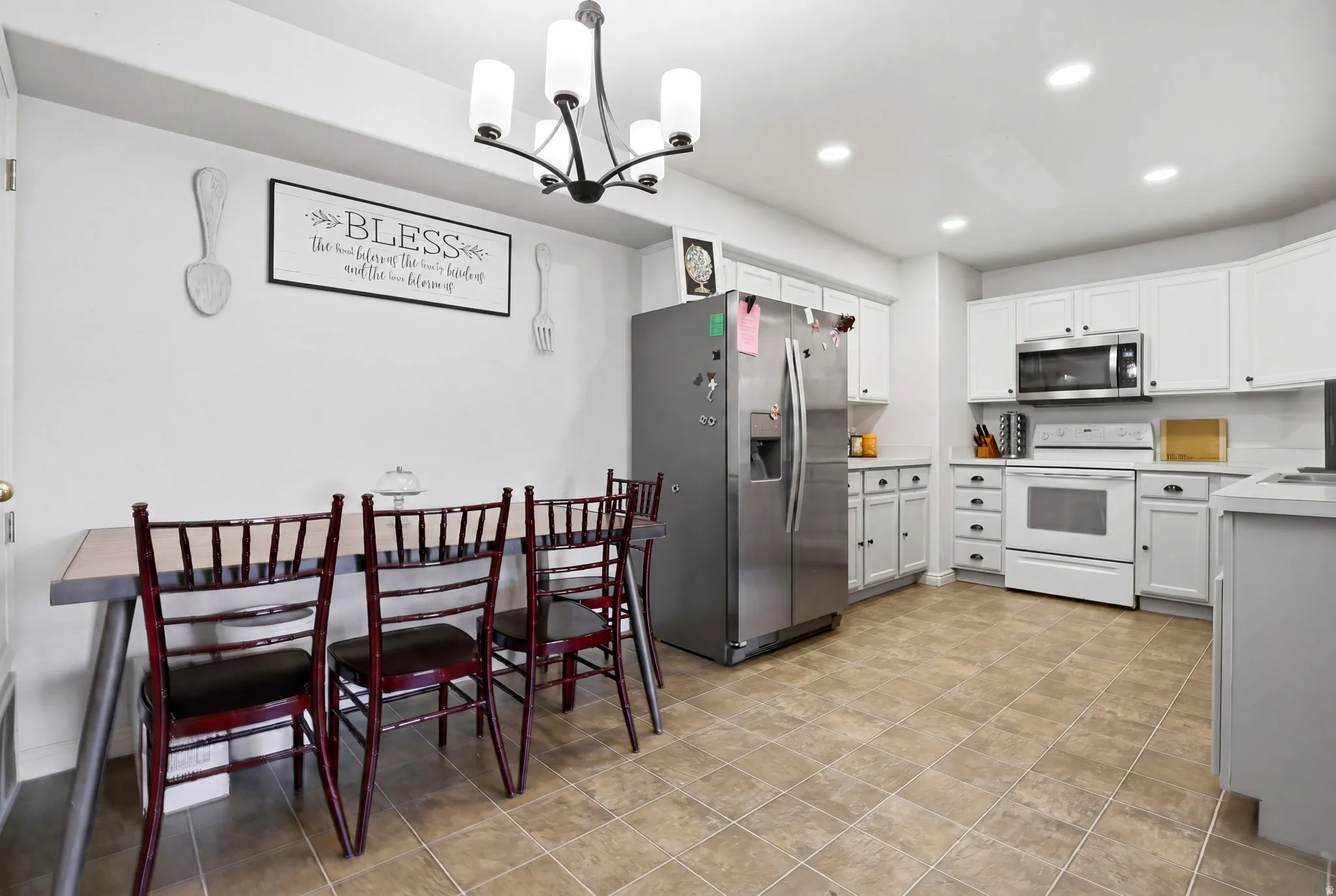 Kitchen featuring light countertops, stainless steel appliances, white cabinetry, and suspended lighting