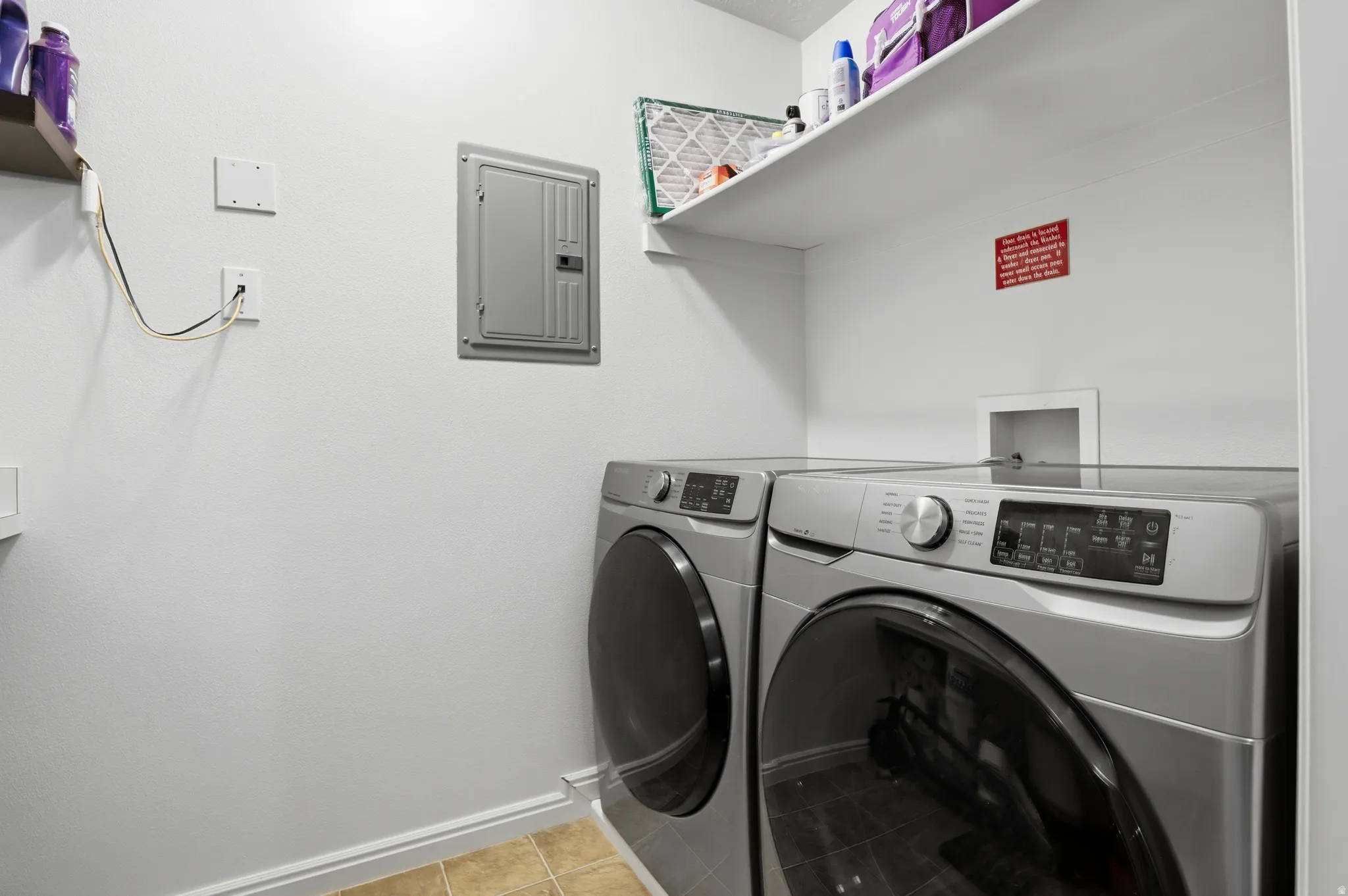 Laundry room featuring electric panel, light tile patterned floors, and washing machine and dryer