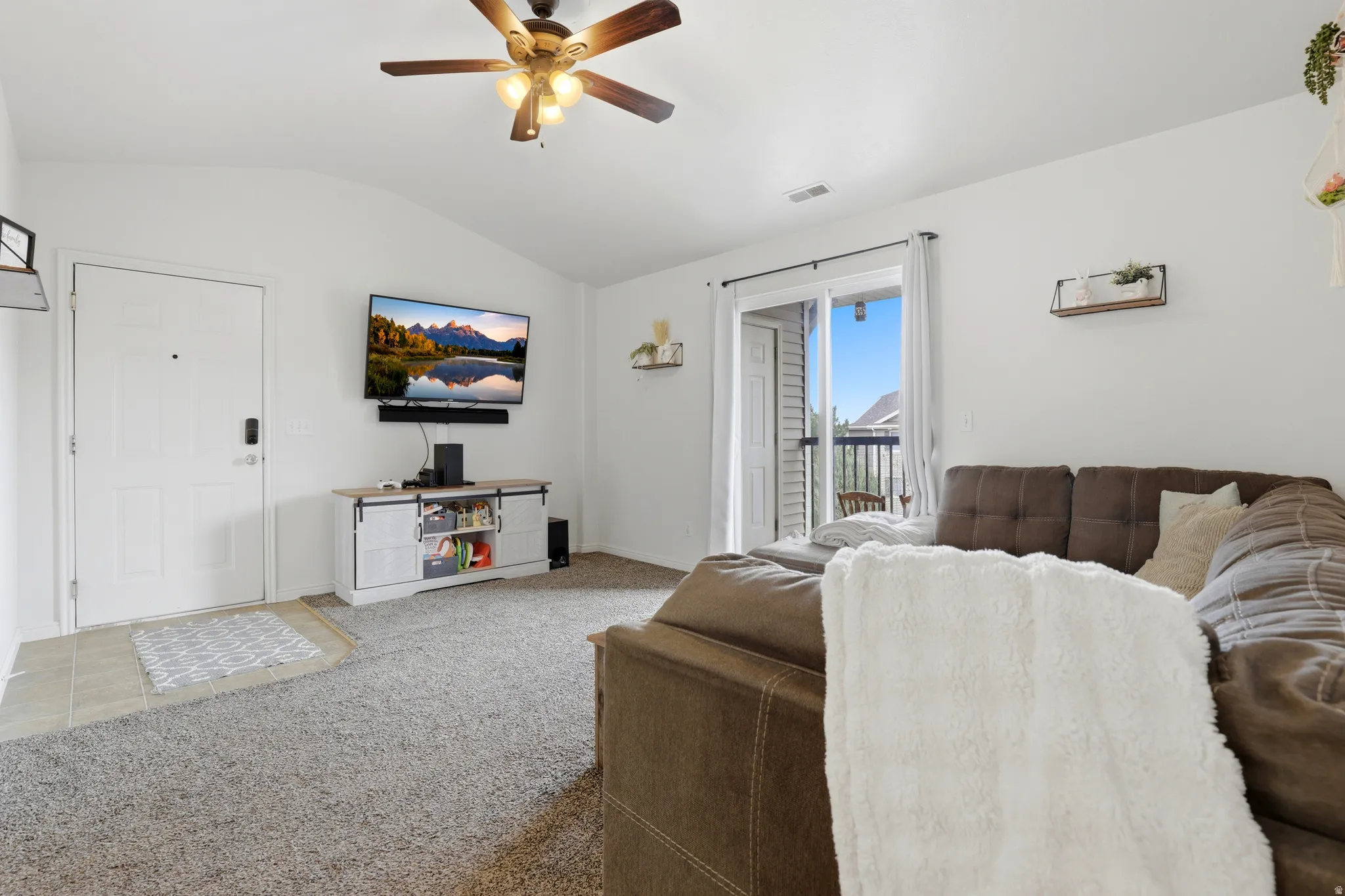 Living room featuring a ceiling fan, carpet floors, and vaulted ceiling