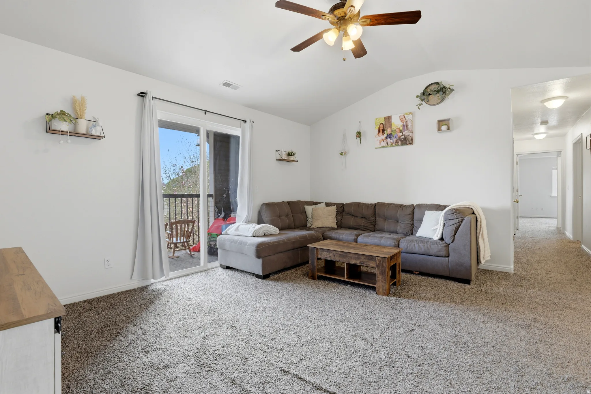 Living room with a ceiling fan, light colored carpet, and lofted ceiling