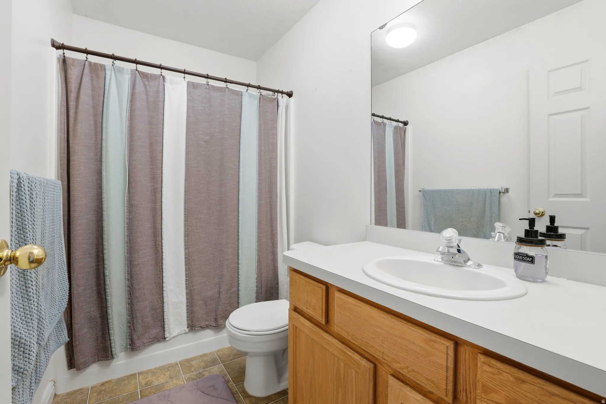Bathroom with vanity, light tile patterned floors, and shower / bathtub combination with curtain