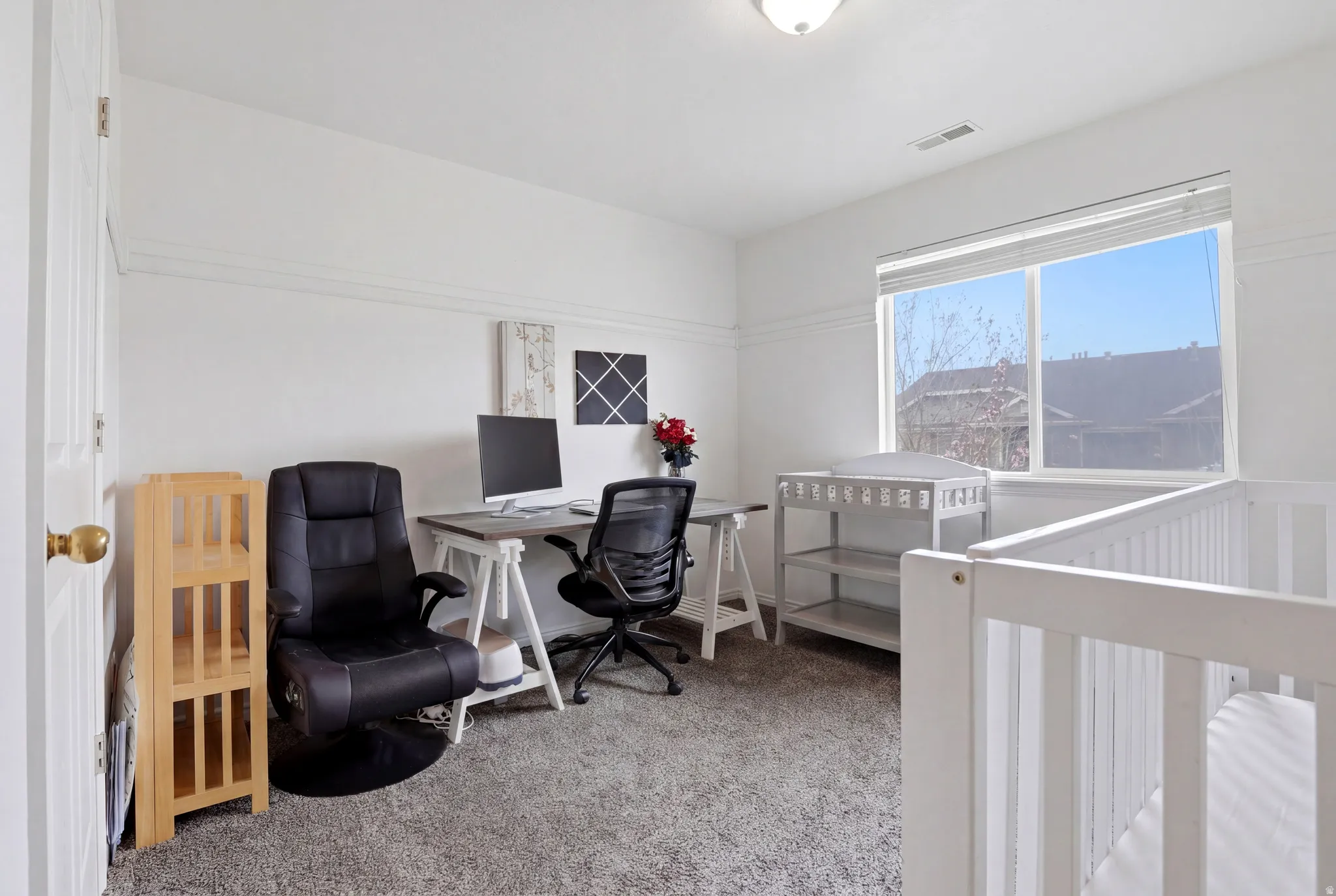 Bedroom featuring light carpet, an office area, and a crib