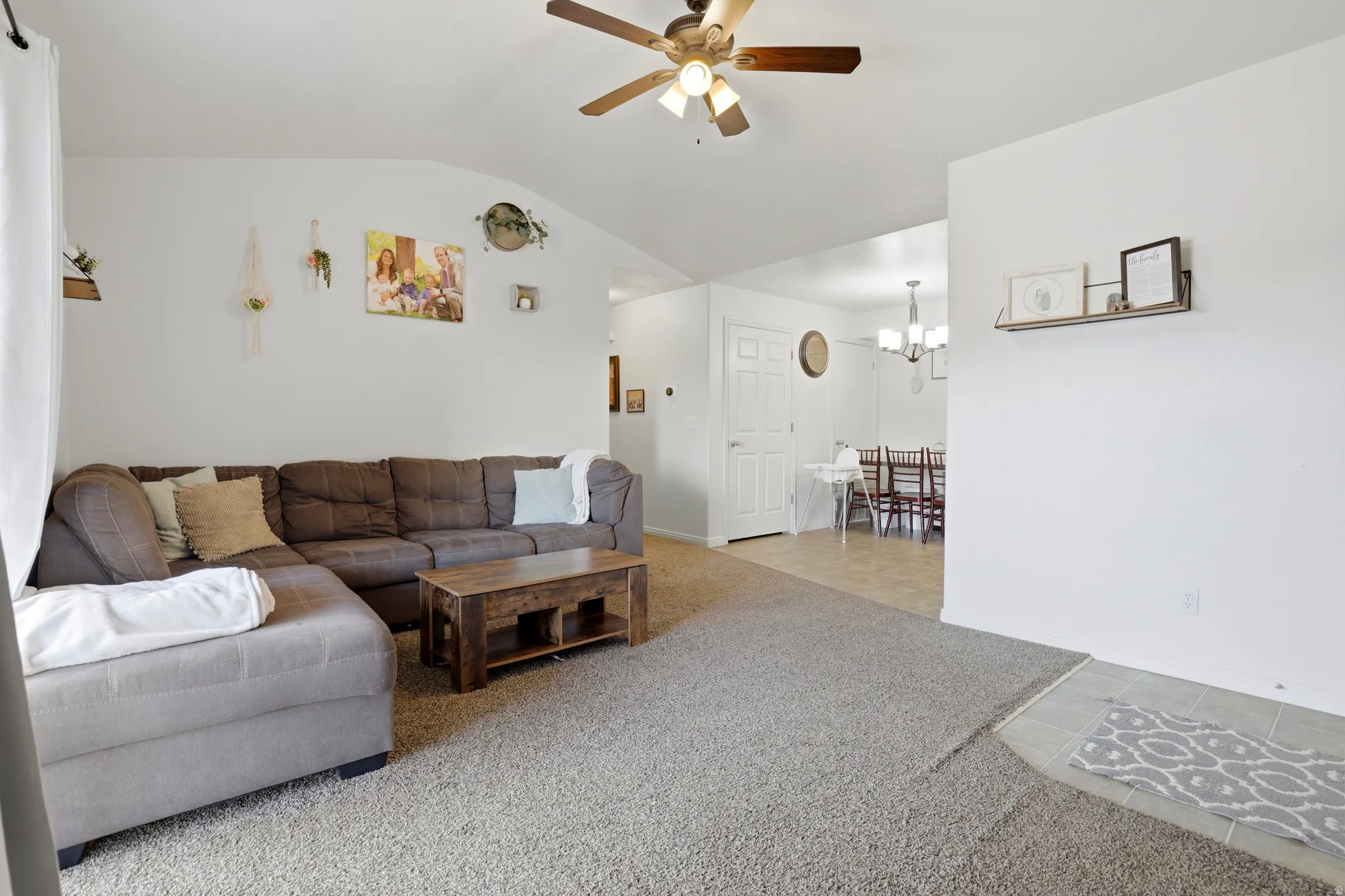 Living room with ceiling fan, light carpet, lofted ceiling, light tile patterned floors, and a chandelier