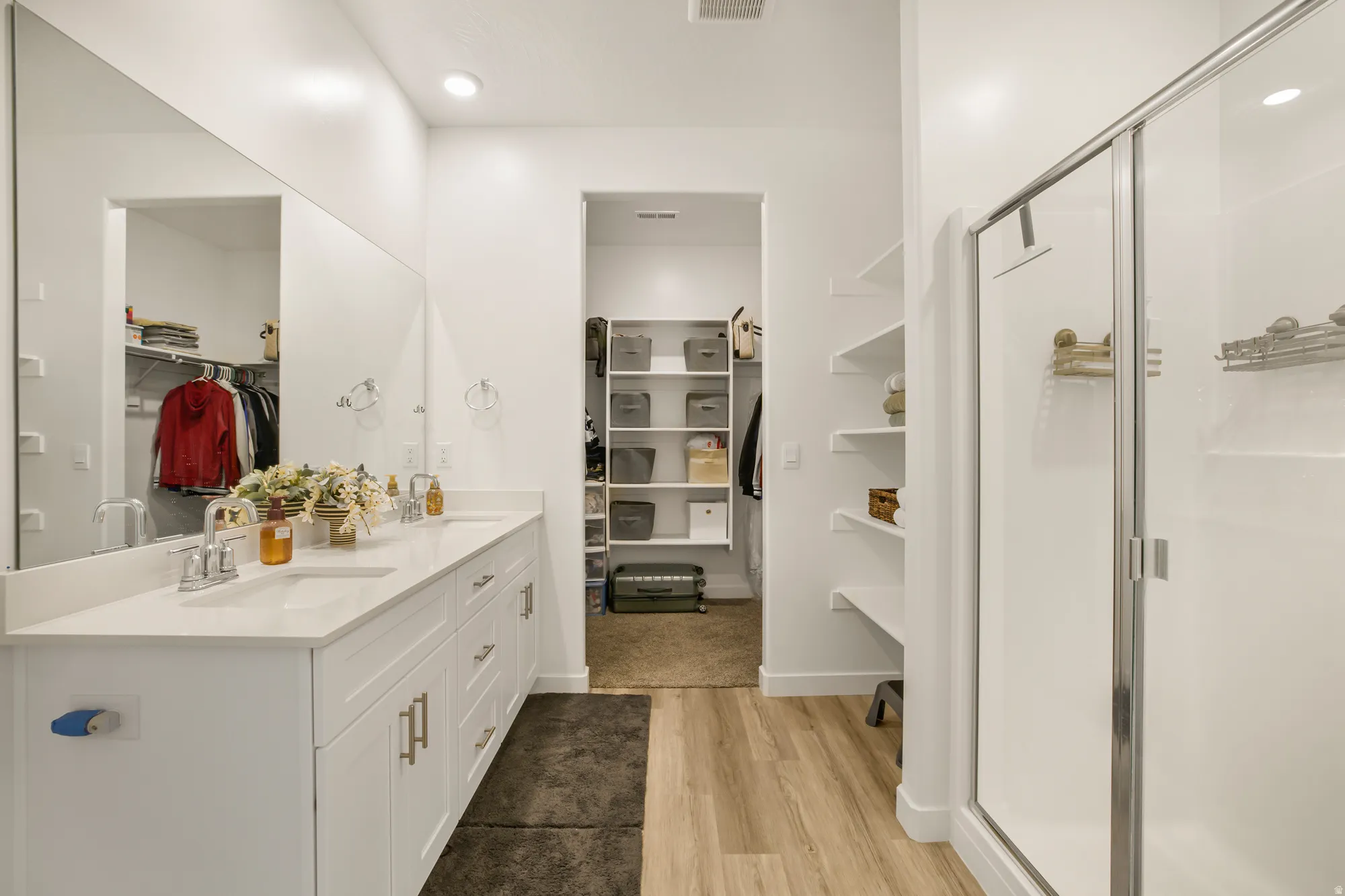 Bathroom featuring a spacious closet, double vanity, a stall shower, and light wood finished floors