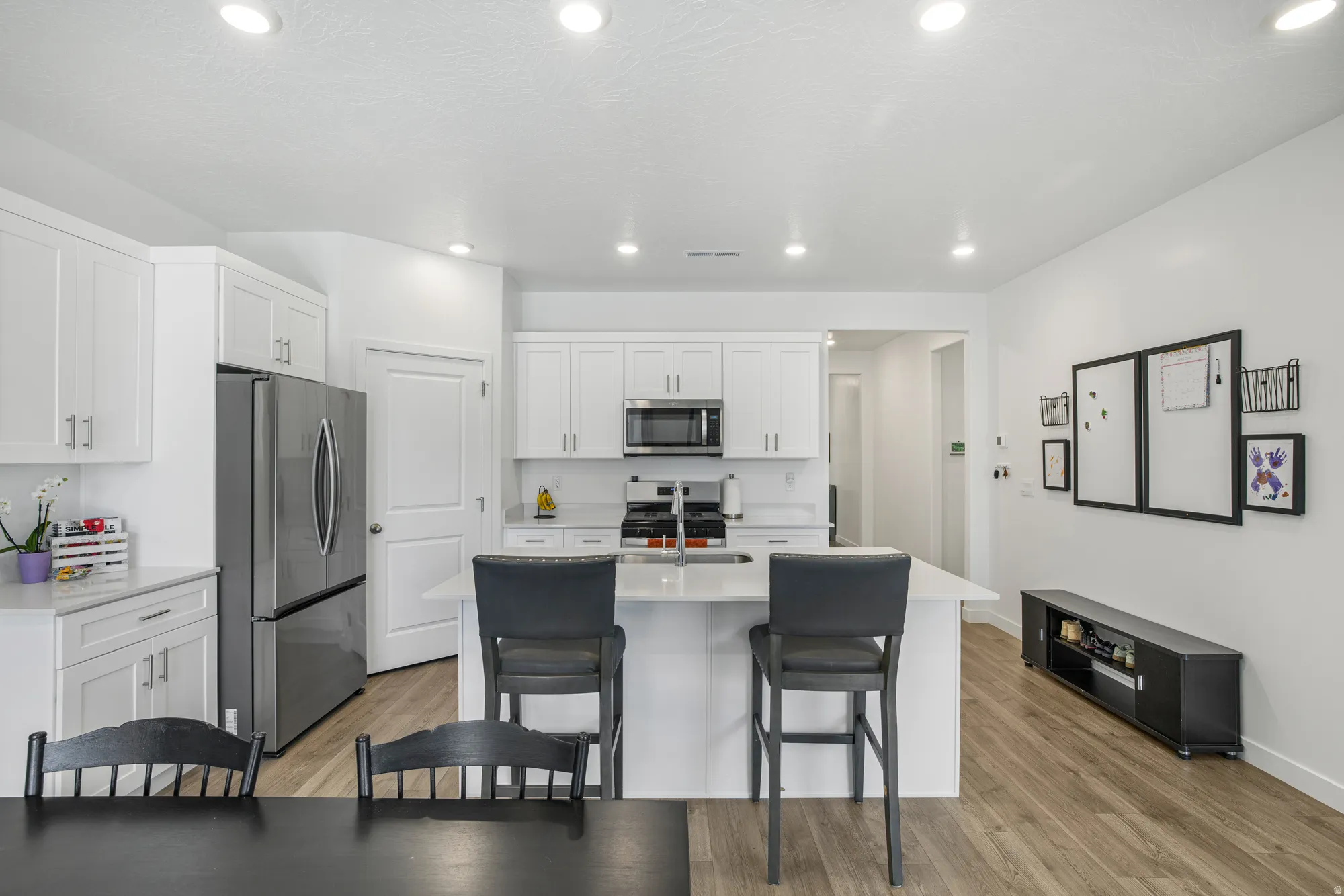 Kitchen featuring stainless steel appliances, white cabinets, light wood-style floors, a center island with sink, and recessed lighting