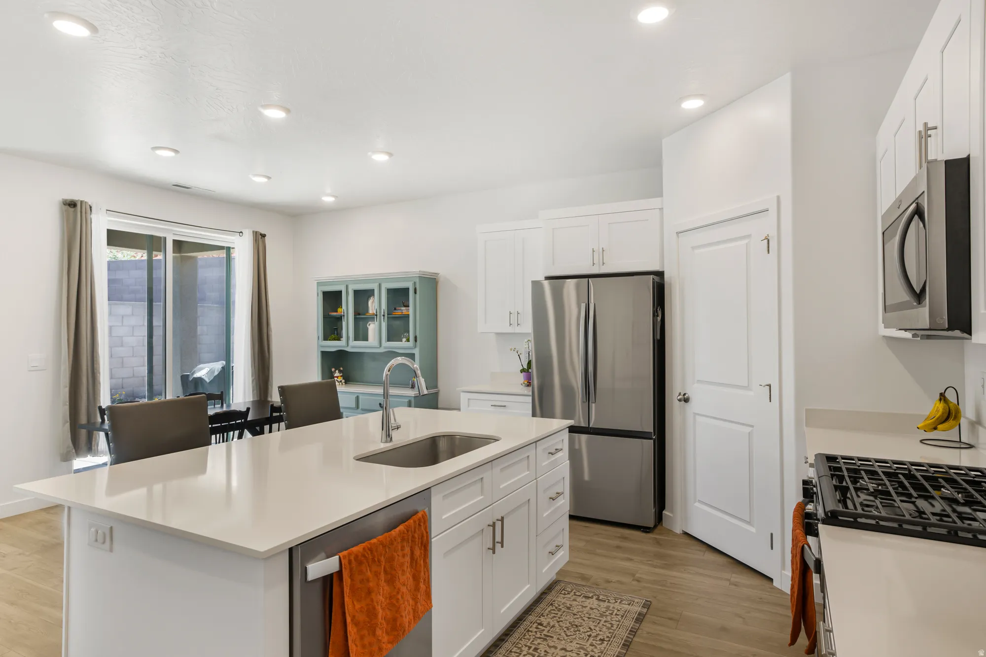 Kitchen featuring stainless steel appliances, white cabinetry, a center island with sink, light wood-style floors, and recessed lighting