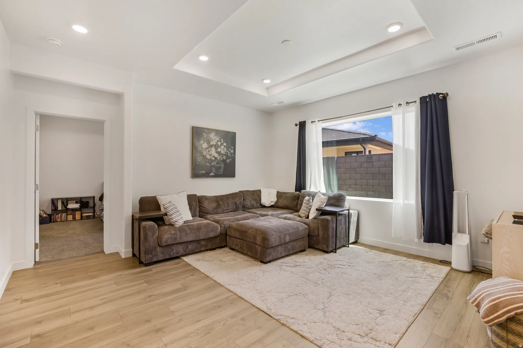 Living room featuring recessed lighting, light wood-style floors, and a raised ceiling