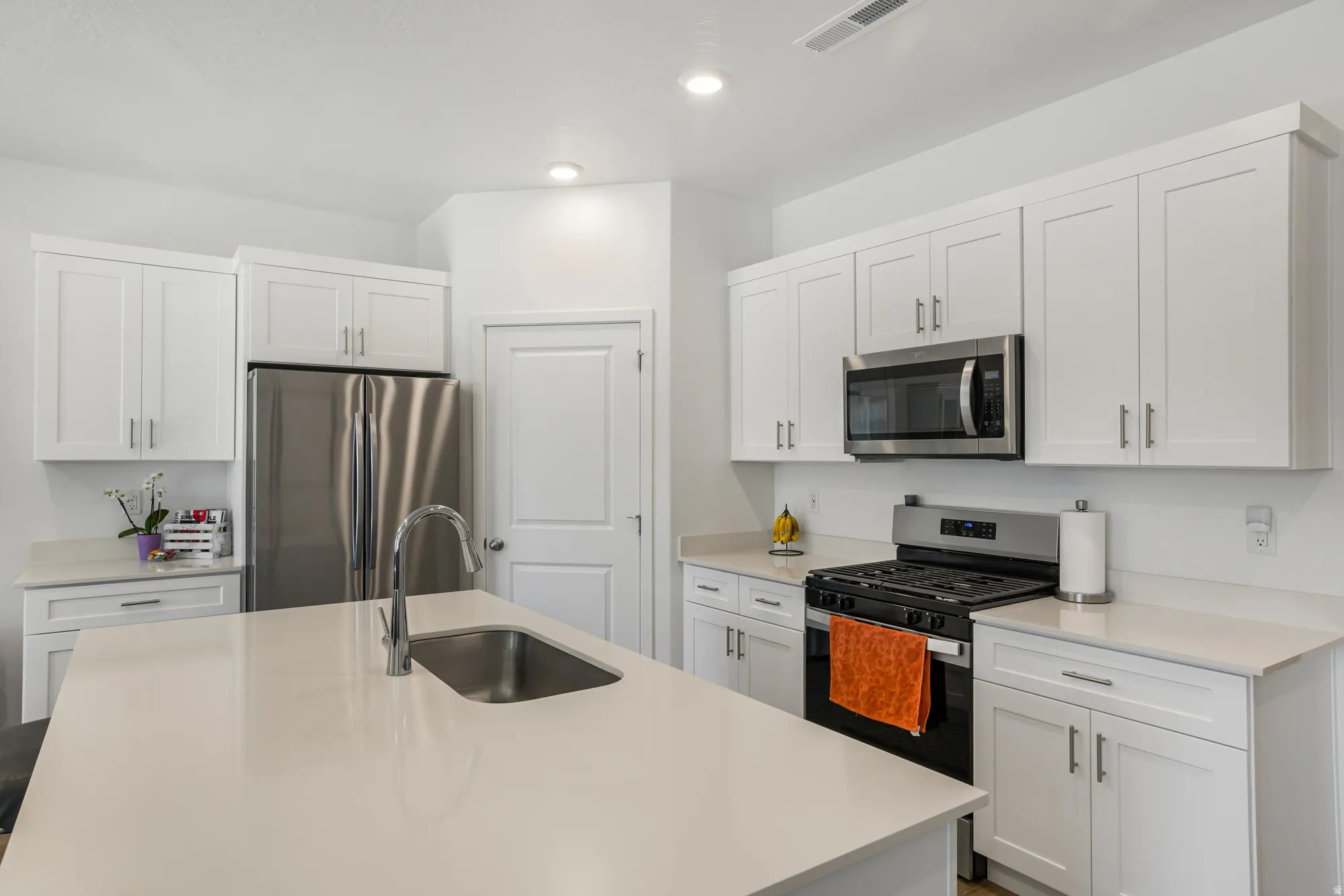 Kitchen featuring stainless steel appliances, white cabinets, a center island with sink, light stone counters, and recessed lighting