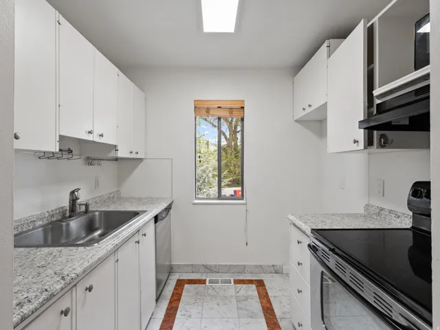 Kitchen featuring inlaid floor details, stainless steel appliances, white cabinetry, and exhaust hood
