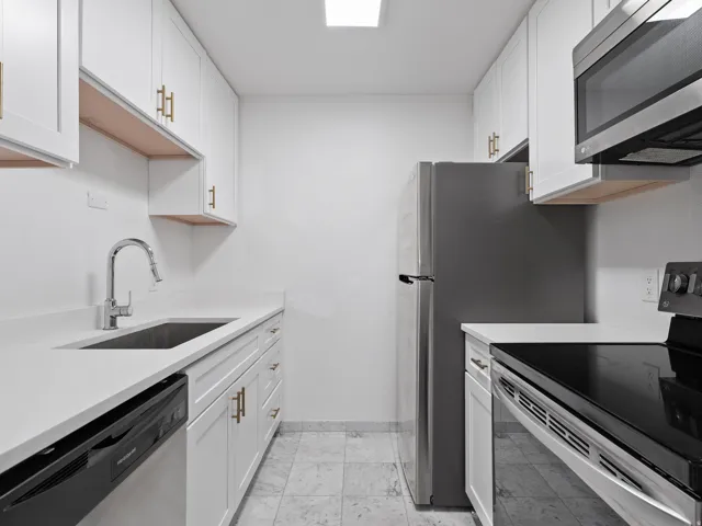 Kitchen with stainless steel appliances, white cabinetry, and light stone counters