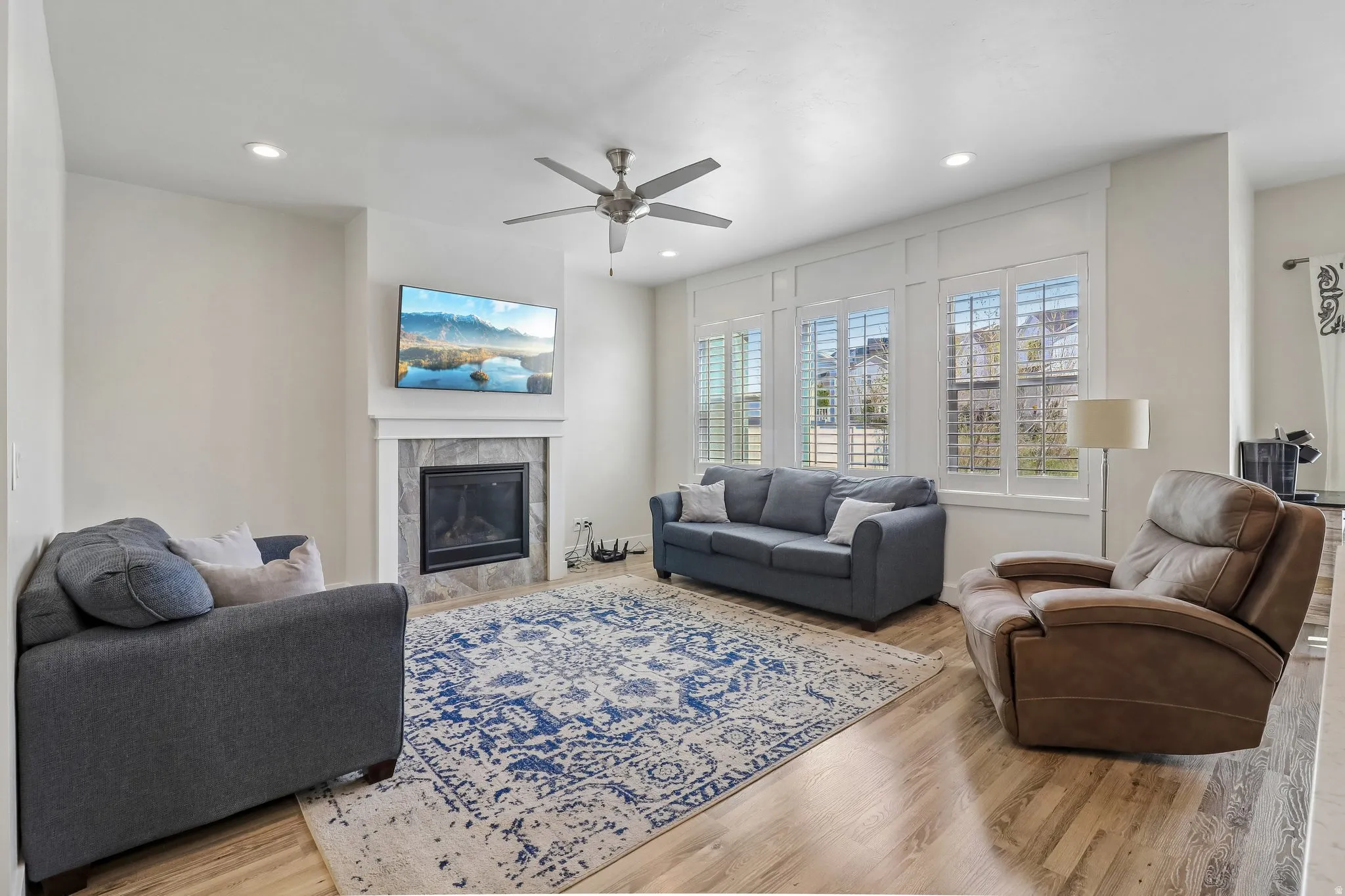 Living room with light wood-style flooring, a tiled fireplace, a ceiling fan, and recessed lighting