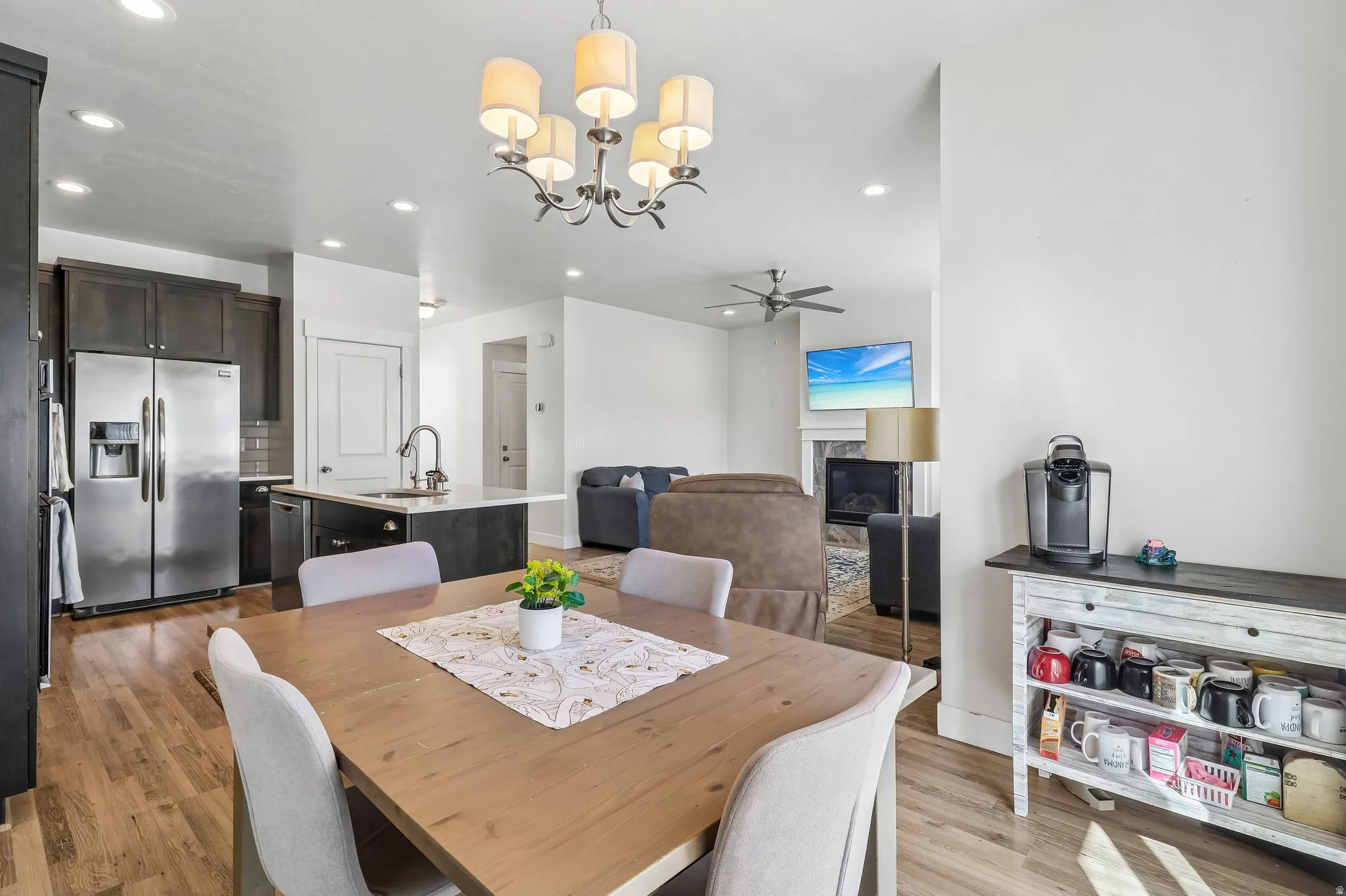 Dining room with light wood-style floors, a glass covered fireplace, suspended lighting, and ceiling fan