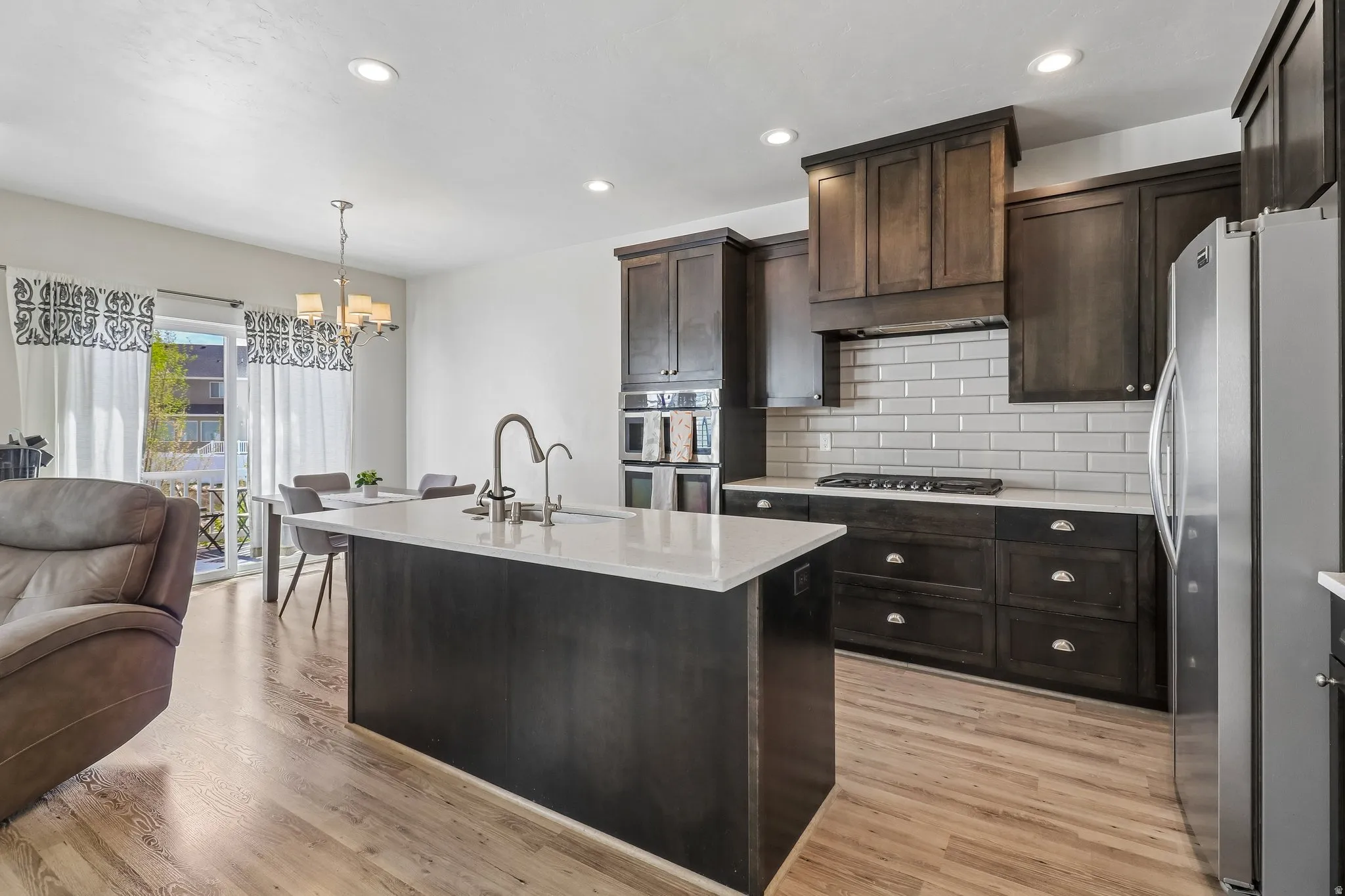 Kitchen with stainless steel appliances, open floor plan, dark wood finish cabinets, light stone countertops, and suspended lighting