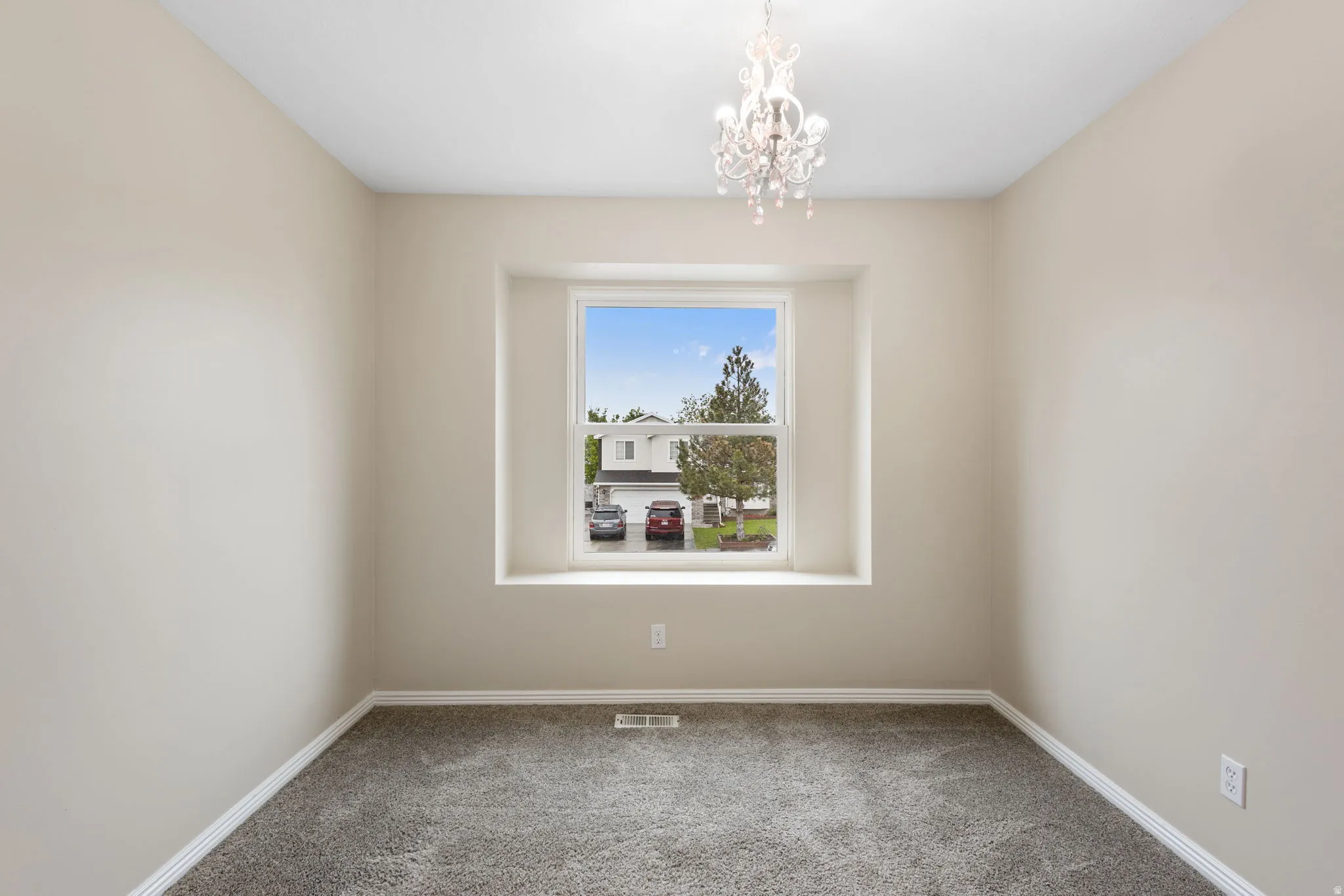 Empty room featuring light colored carpet and hanging lights