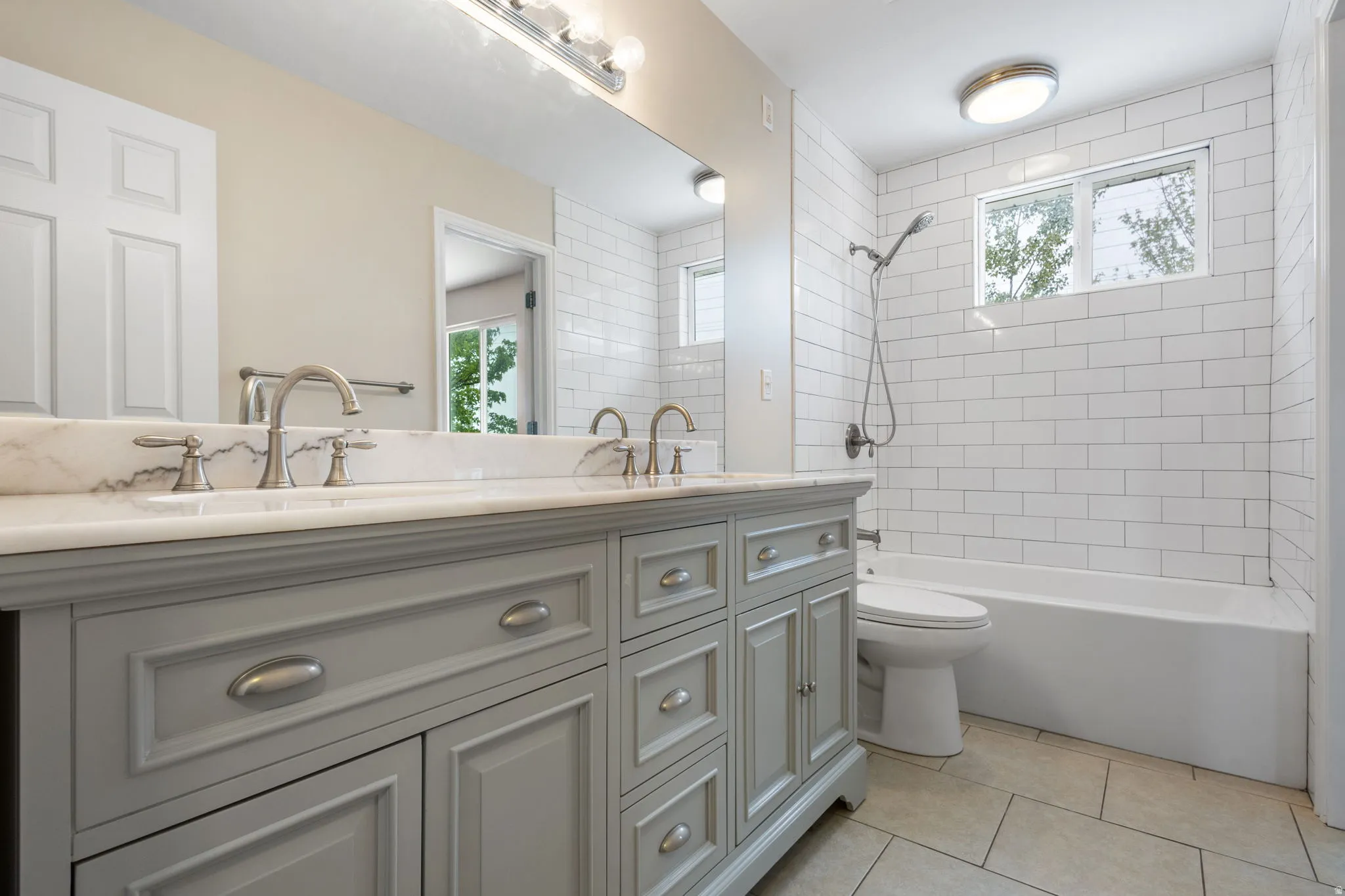 Bathroom featuring double vanity, plenty of natural light, light tile patterned flooring, and bathing tub / shower combination